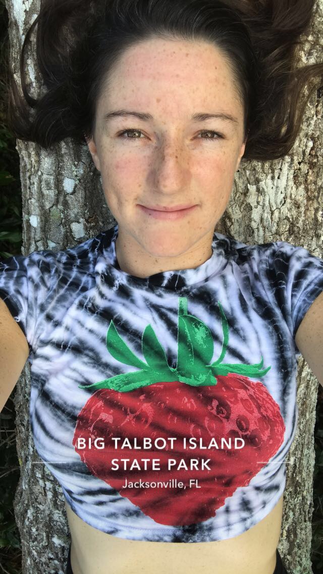 Taya smiling in the sun, lying against a mossy tree trunk